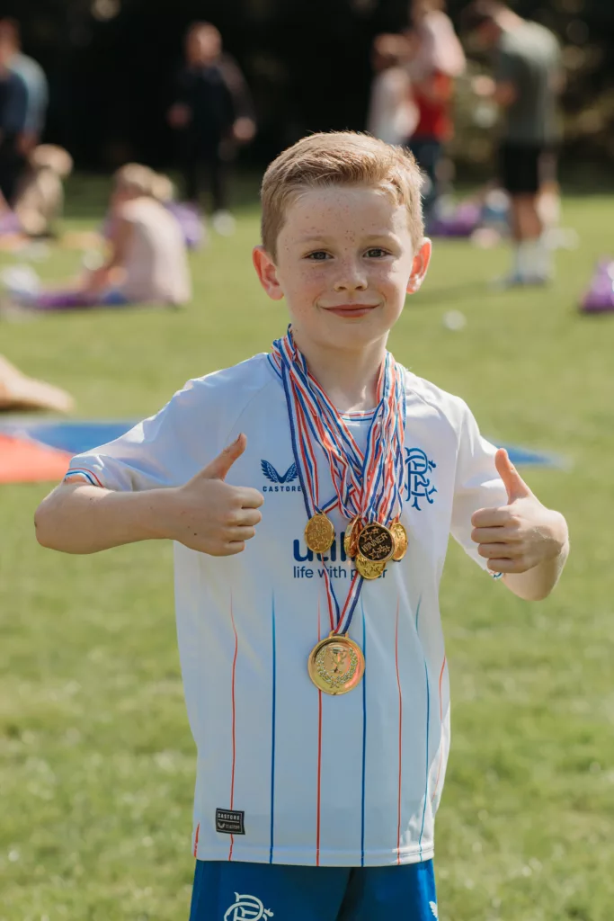 young boy with double thumbs up and medals