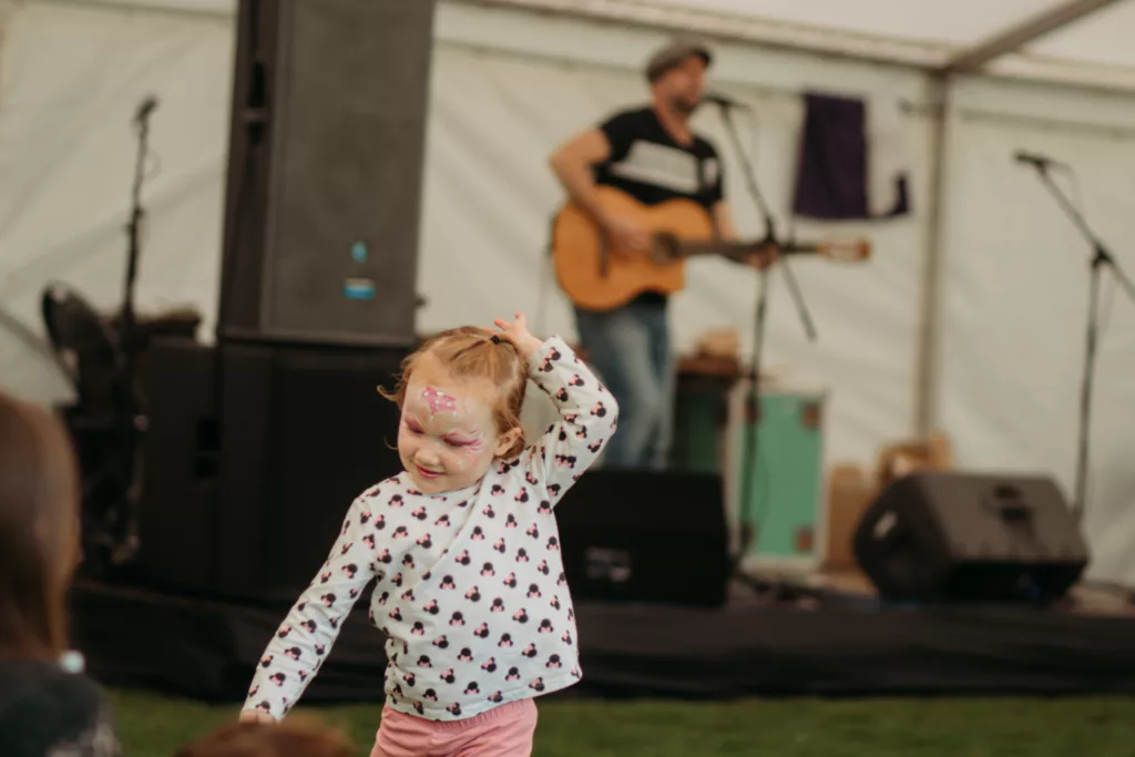 girl dancing to music, stage and guitar player/singer in background
